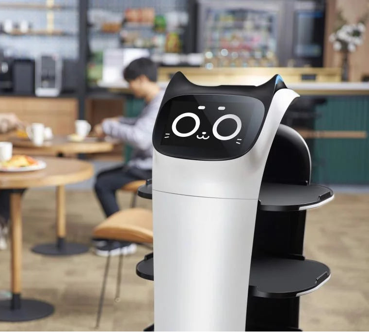 BellaBot Pro im Gastronomieeinsatz mit Tabletts und Display Gesicht zwischen Gästen im Restaurant