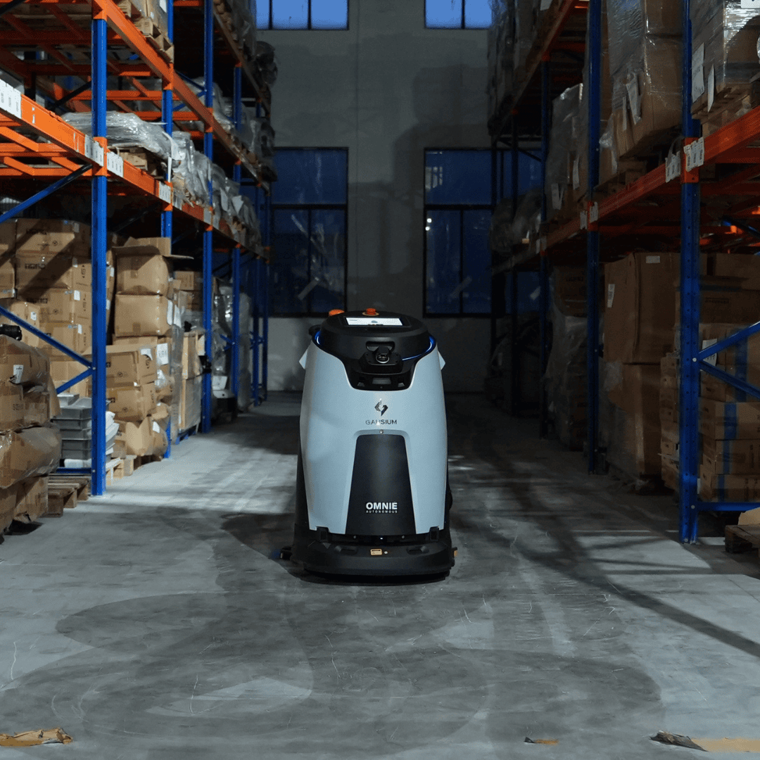 Autonomer Omnie Roboter reinigt die Lagerhalle zwischen hohen Regalen voller Kartons präzise