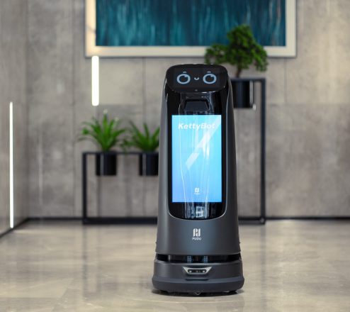 KettyBot Serviceroboter mit Display steht in einem modernen Empfangsbereich mit Pflanzen.