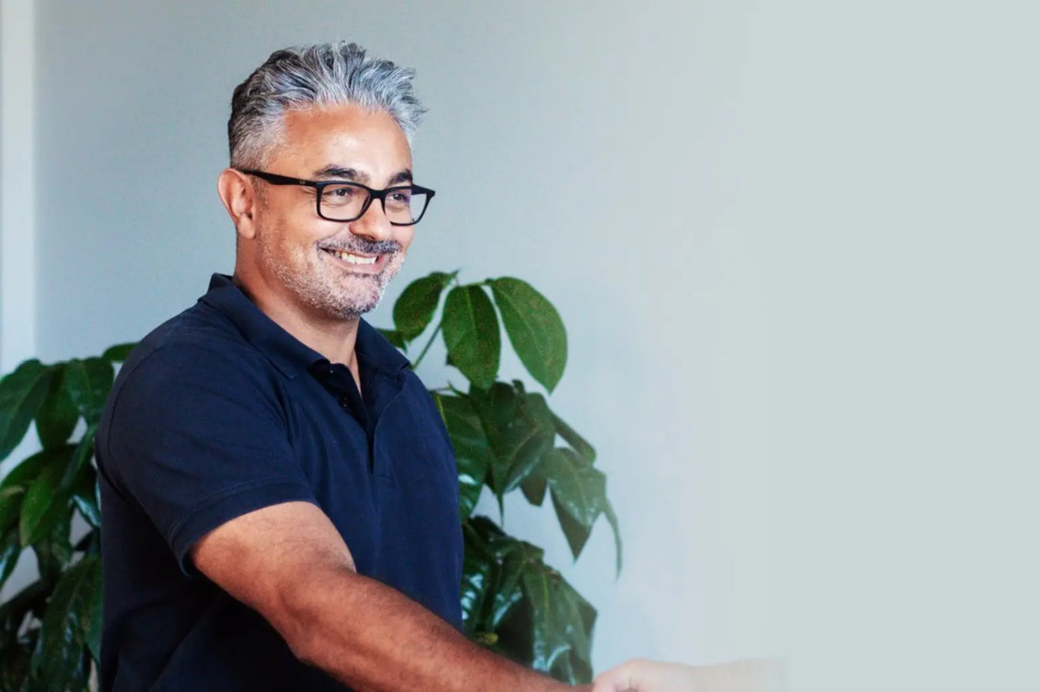 Geschäftsmann mit Brille und Bart im Gespräch beim Händedruck vor Pflanze in moderner Büroatmosphäre