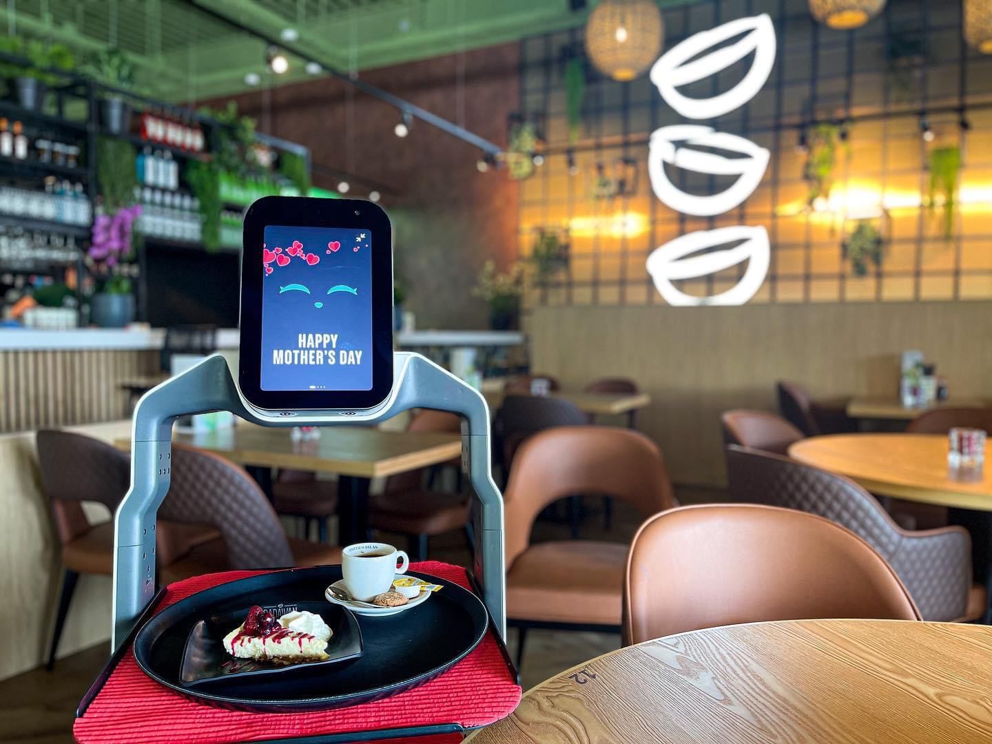 Serviceroboter präsentiert Dessert und Kaffee auf Tablett mit Muttertagsgrafik im modernen Café