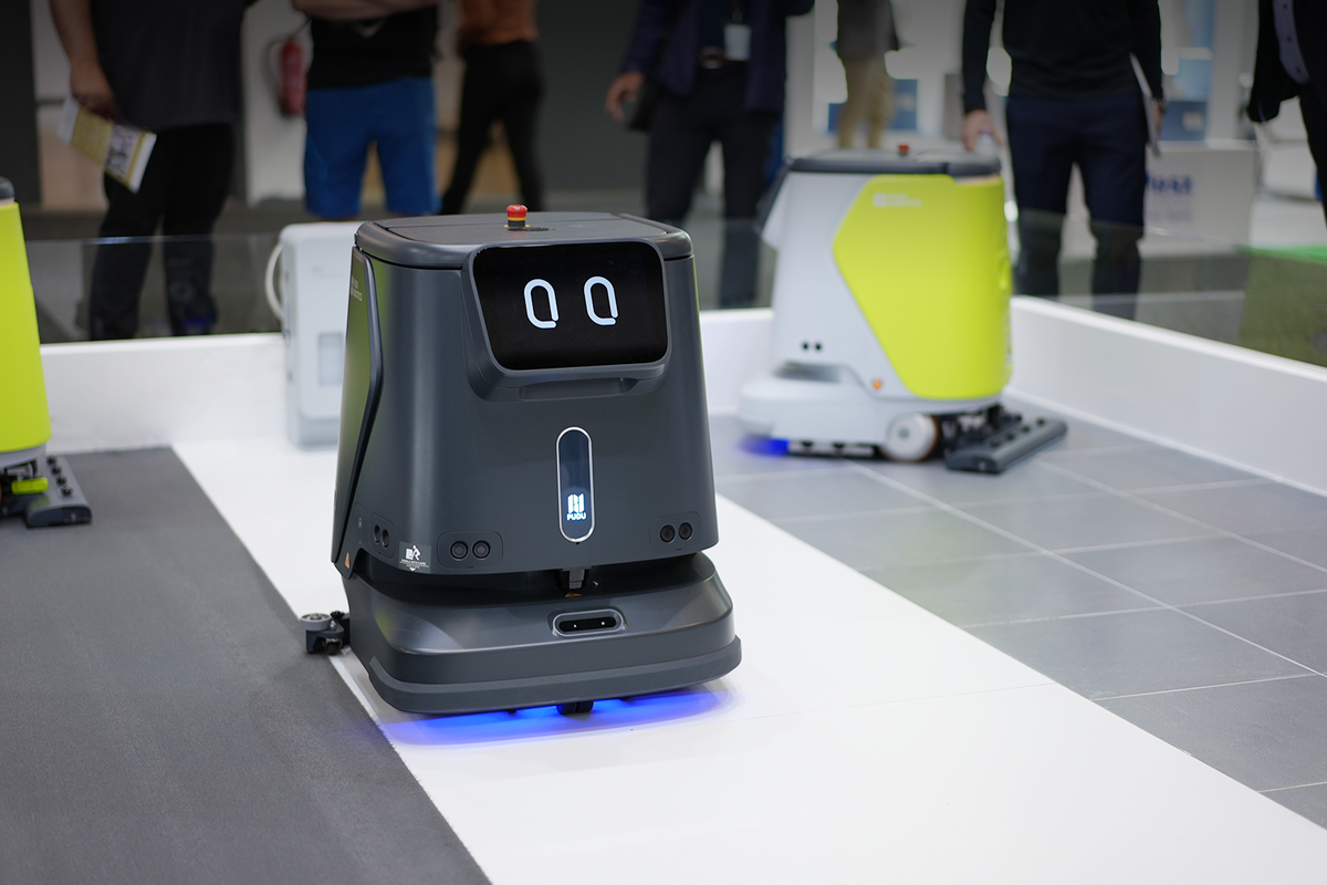 Pudu CC1 Reinigungsroboter in Schwarz im Einsatzbereich auf Messe mit weiteren Robotermodellen