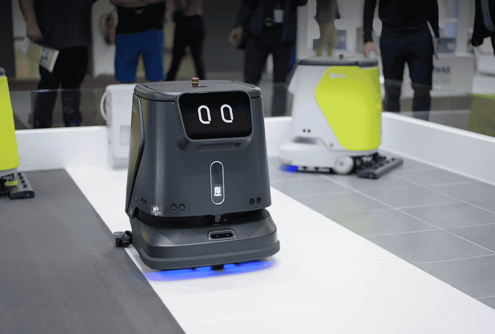 Pudu CC1 Reinigungsroboter in Schwarz im Einsatzbereich auf Messe mit weiteren Robotermodellen