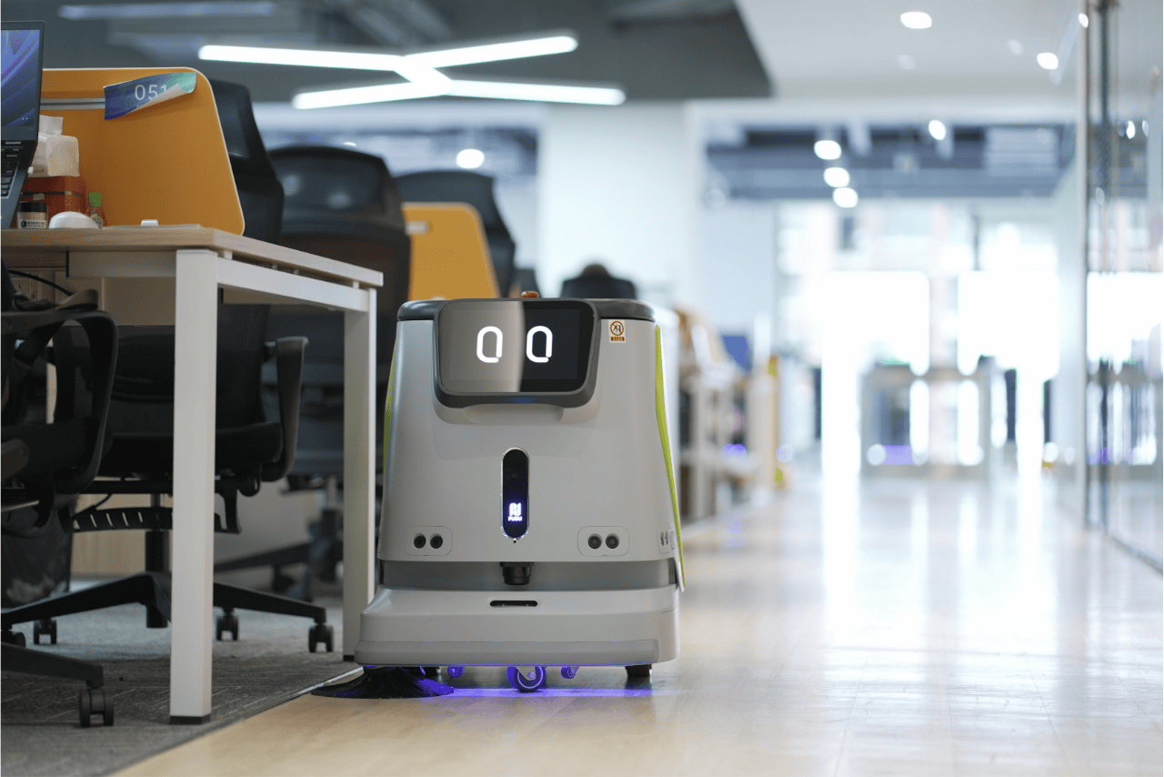 Autonomer Reinigungsroboter fährt durch modernes Büro mit Schreibtischen und Glasfronten