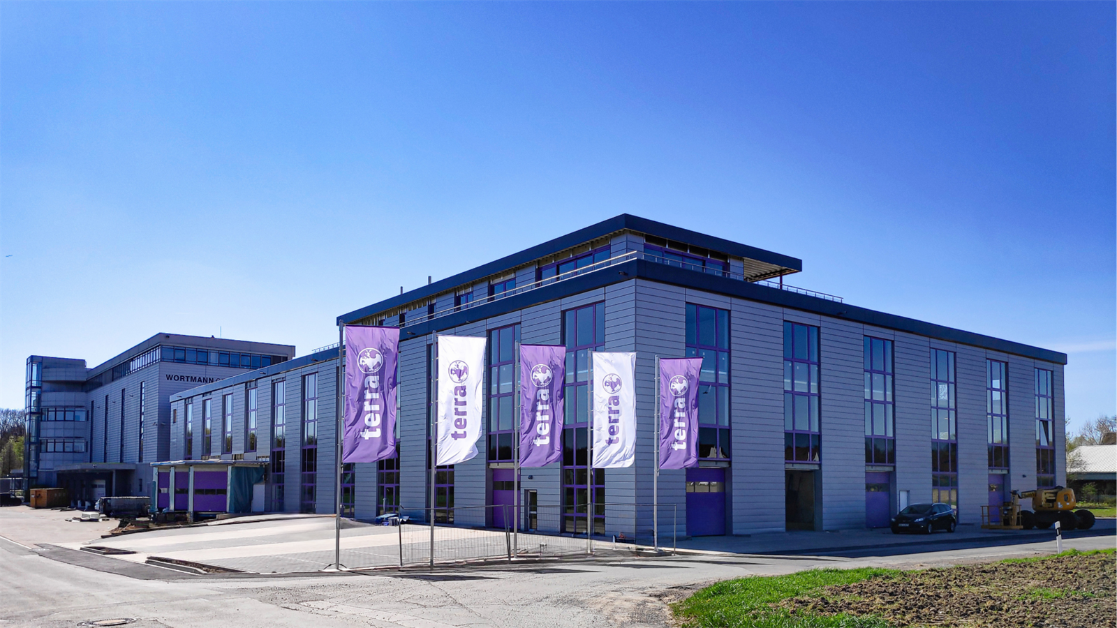 Terra Firmengebaeude mit lila und weißen Terra Robotics Flaggen unter klarem blauem Himmel