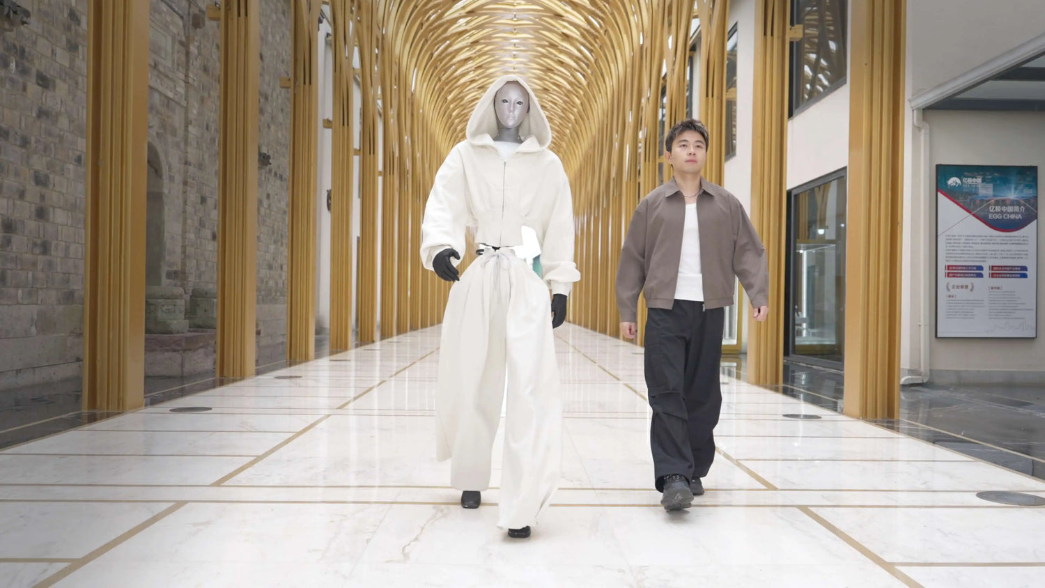 Humanoider Roboter Unitree H2 im weißen Fashion Outfit schreitet neben Mensch durch moderne Galerie