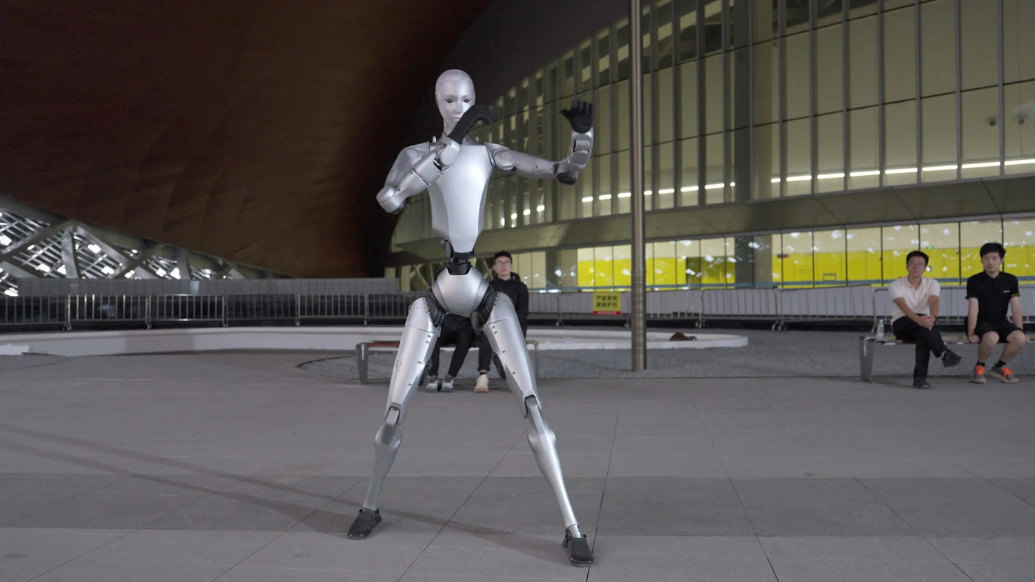 Humanoider Roboter Unitree H2 demonstriert dynamische Kampfpose vor moderner Architektur im Außenbereich