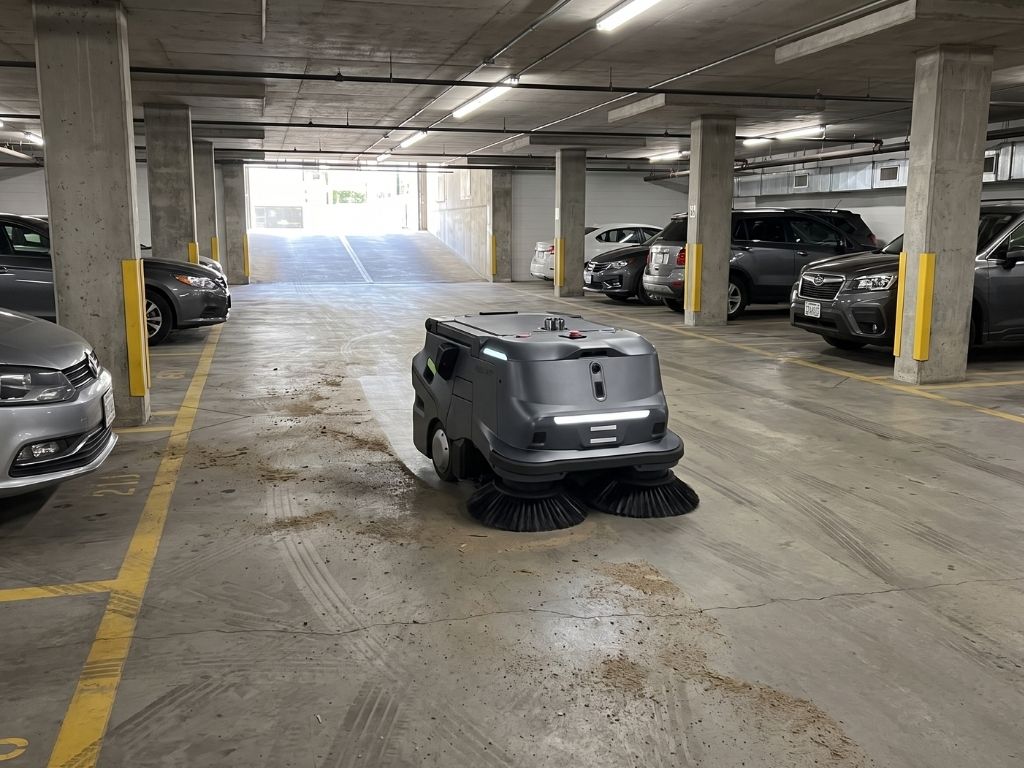 Autonomer Reinigungsroboter bei der Bodenreinigung in einem Parkhaus mit geparkten Fahrzeugen